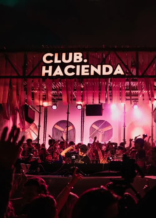 DJ-podium met verlicht Club Hacienda-bord en juichend publiek op een feest