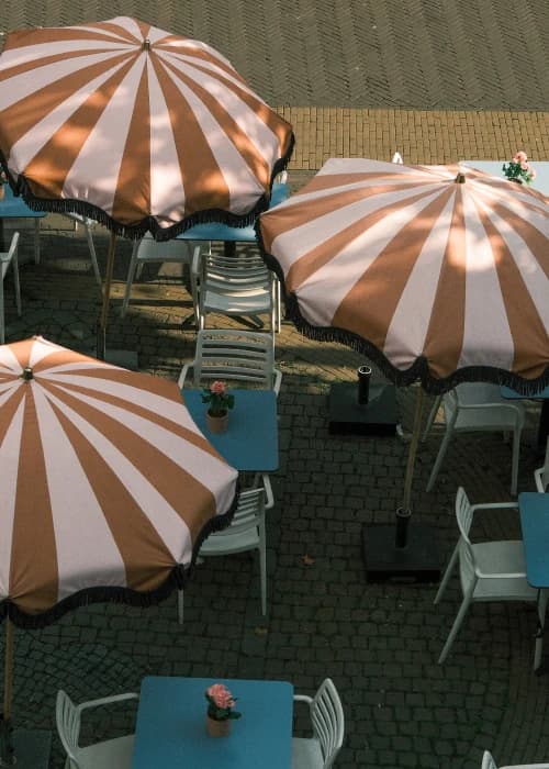 Terras van MILK met bruin-wit gestreepte parasols en blauwe tafels, van boven gezien